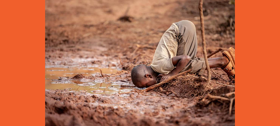 african boy drinking from a puddle